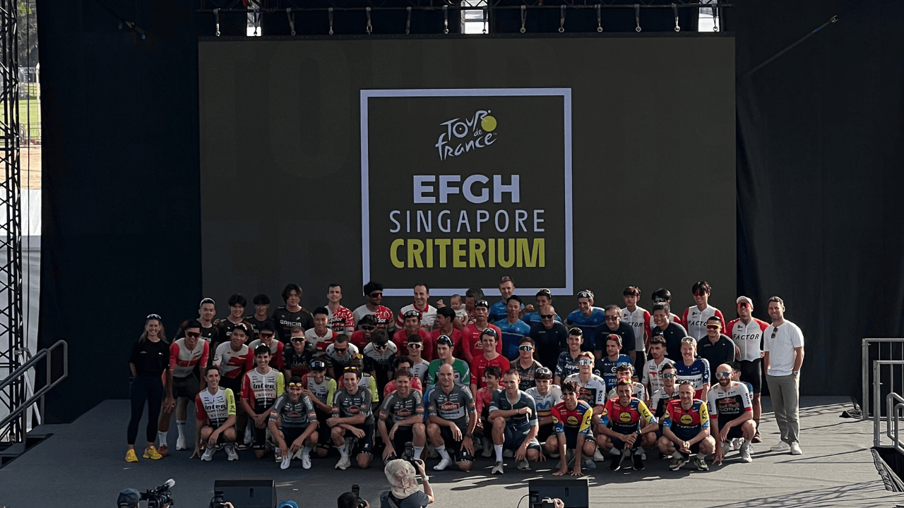 Professional cyclists on stage in front of the Tour de France EFGH Singapore Criterium backdrop, with EFGH as the title sponsor.